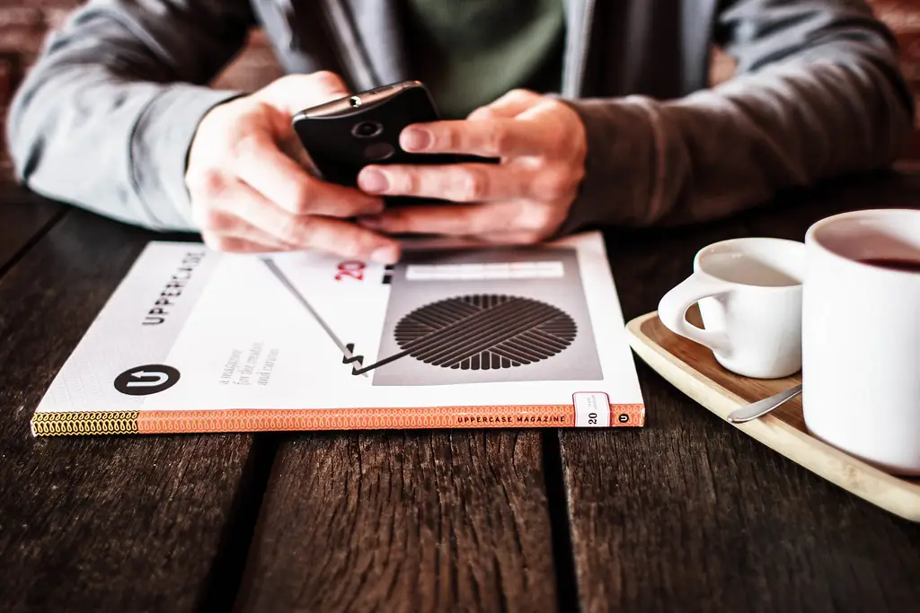 Mains tenant un smartphone au-dessus d'une table, à côté d'une tasse de café